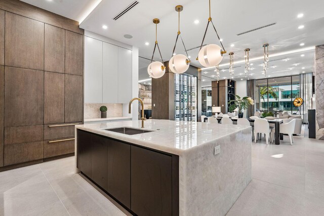 kitchen featuring white cabinetry, sink, light stone counters, a large island with sink, and pendant lighting