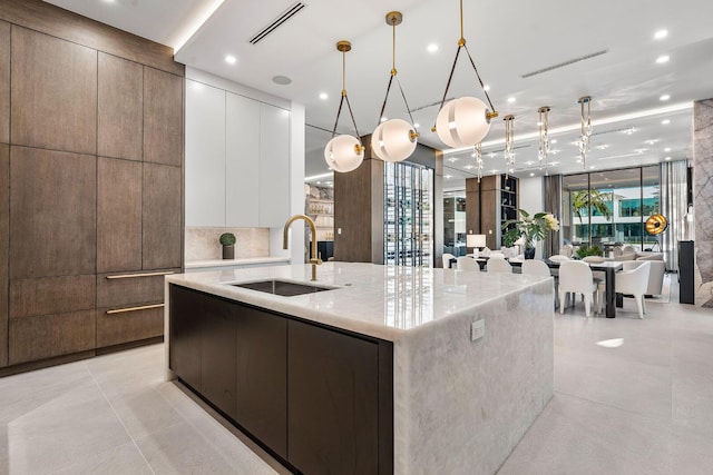 kitchen with sink, white cabinetry, light stone counters, hanging light fixtures, and a large island