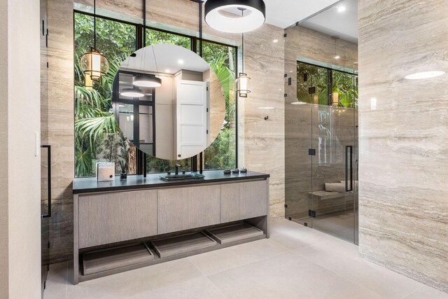 bathroom featuring tile patterned flooring, vanity, a shower with door, and tile walls