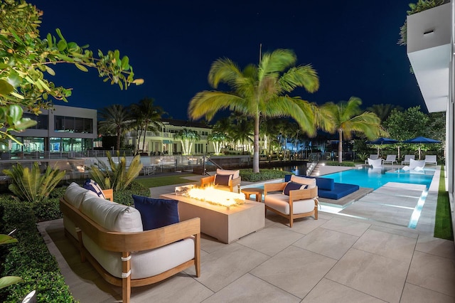 pool at twilight featuring a patio area and an outdoor living space with a fire pit