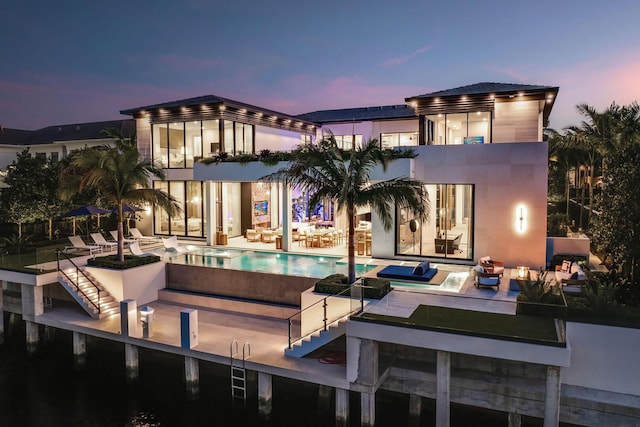 back house at dusk featuring a patio area and a swimming pool with hot tub