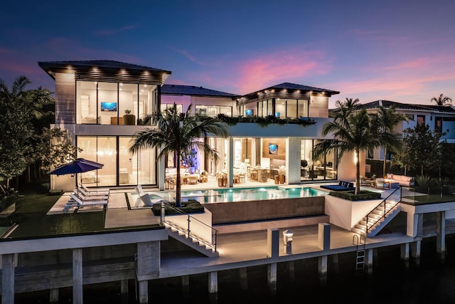 back house at dusk featuring a swimming pool with hot tub and a patio area