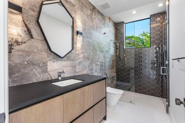 bathroom with a tile shower, vanity, tile walls, tile patterned flooring, and toilet