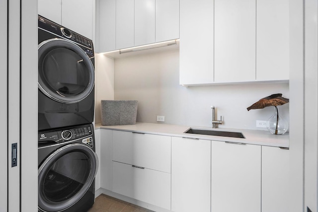 laundry area with cabinets, stacked washing maching and dryer, and sink