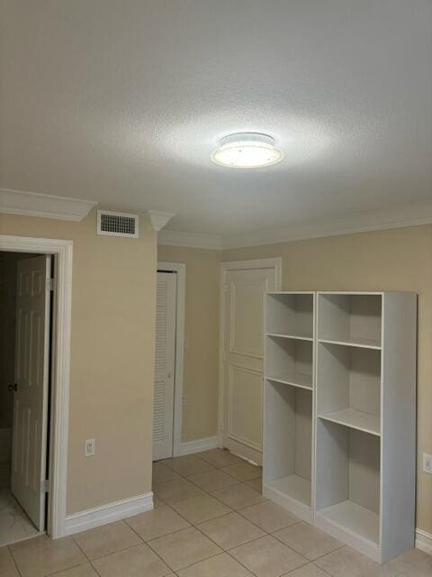 interior space with a textured ceiling, light tile patterned flooring, and crown molding