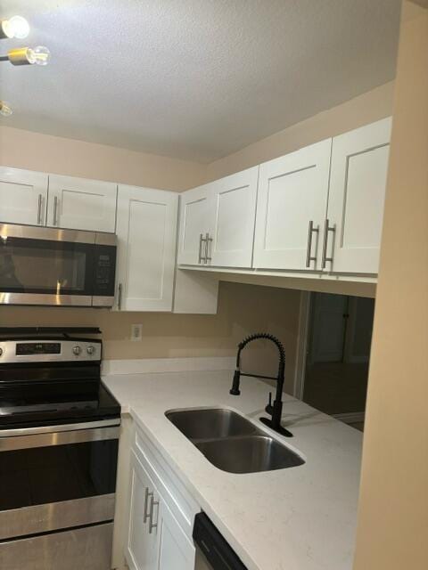 kitchen with white cabinetry, sink, light stone counters, a textured ceiling, and appliances with stainless steel finishes