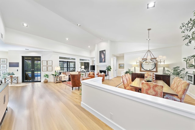 living room with french doors, light wood-type flooring, lofted ceiling, and a notable chandelier