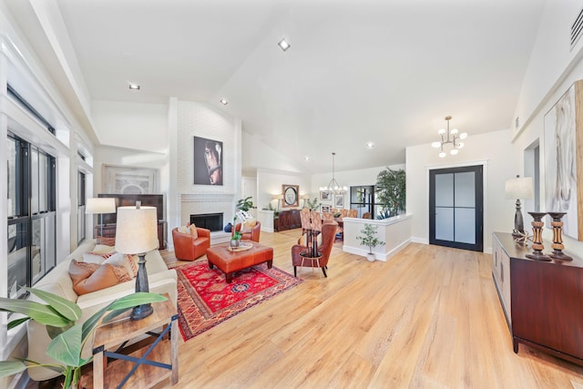 living room with light hardwood / wood-style floors, a chandelier, vaulted ceiling, and a brick fireplace