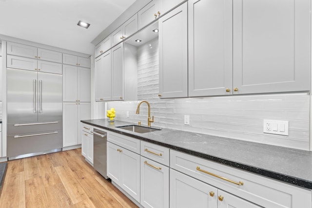 kitchen featuring backsplash, dark stone counters, sink, built in refrigerator, and light wood-type flooring