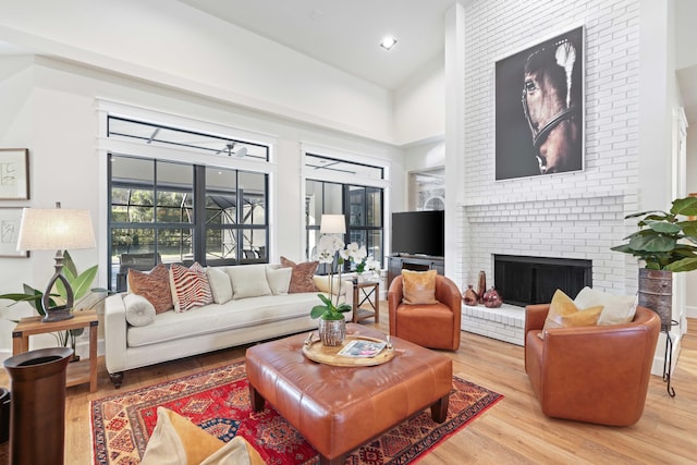 living room featuring light hardwood / wood-style floors, a high ceiling, and a brick fireplace