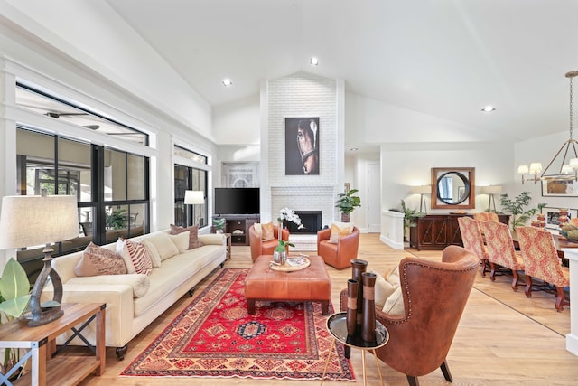 living room featuring light wood-type flooring, an inviting chandelier, a brick fireplace, and lofted ceiling