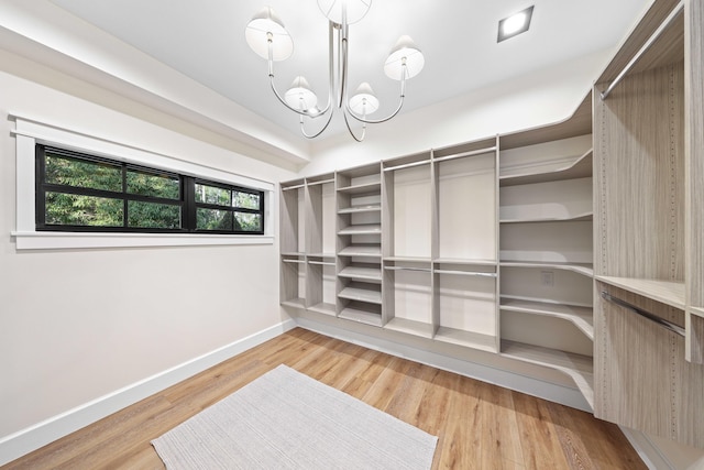 walk in closet with light hardwood / wood-style flooring and an inviting chandelier