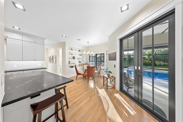 kitchen with light wood-type flooring, pendant lighting, dark stone countertops, a chandelier, and white cabinetry