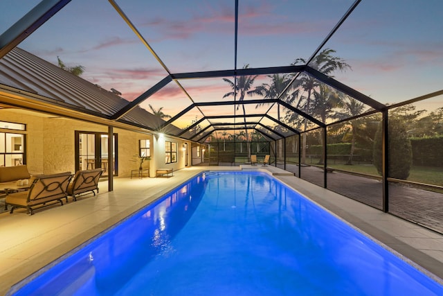 pool at dusk featuring glass enclosure and a patio area