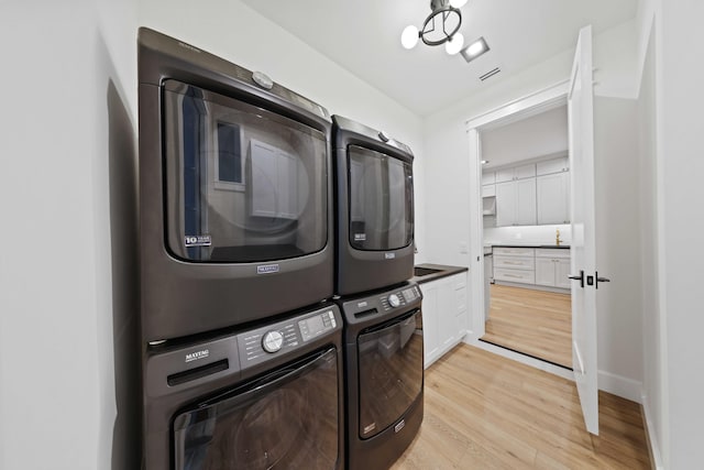 washroom featuring cabinets, light hardwood / wood-style flooring, and stacked washing maching and dryer