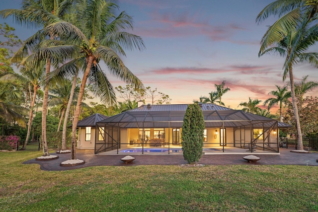 back house at dusk featuring a lawn and a lanai