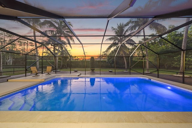 pool at dusk featuring glass enclosure and a patio area