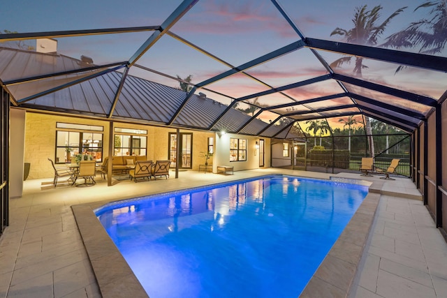 pool at dusk with outdoor lounge area, a patio, and a lanai