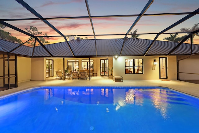 pool at dusk with glass enclosure and a patio area