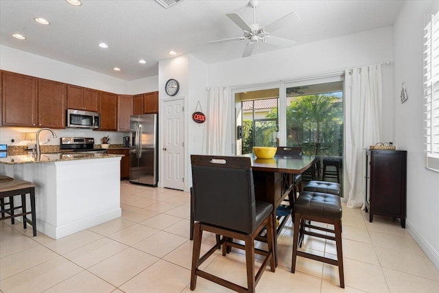 kitchen featuring a breakfast bar, light stone countertops, appliances with stainless steel finishes, light tile patterned flooring, and kitchen peninsula