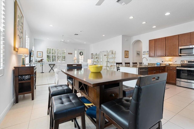 kitchen featuring ceiling fan, a center island with sink, light tile patterned flooring, and stainless steel appliances