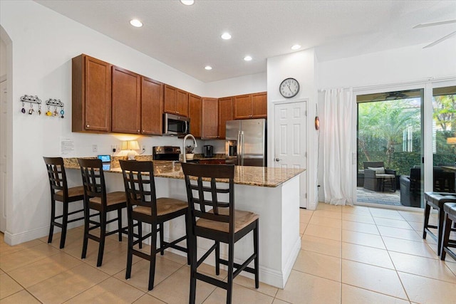 kitchen featuring stainless steel appliances, kitchen peninsula, stone countertops, a breakfast bar area, and light tile patterned floors