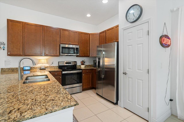 kitchen featuring kitchen peninsula, light stone counters, stainless steel appliances, sink, and light tile patterned floors