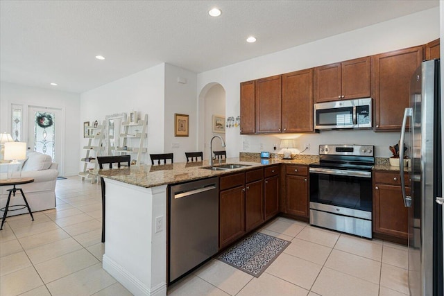 kitchen featuring sink, stainless steel appliances, light stone counters, kitchen peninsula, and light tile patterned floors