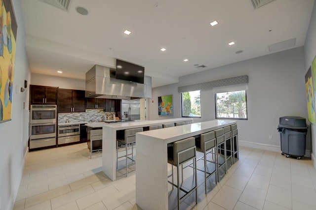 kitchen with decorative backsplash, a large island, a breakfast bar, and dark brown cabinetry