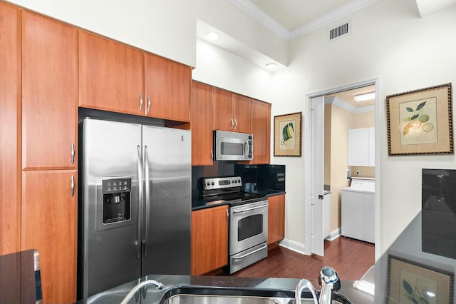 kitchen with appliances with stainless steel finishes, dark hardwood / wood-style flooring, crown molding, and washer / dryer