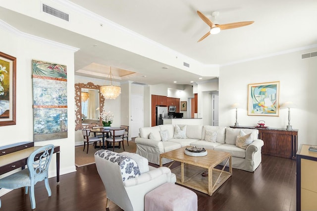 living room featuring ceiling fan with notable chandelier, dark hardwood / wood-style flooring, crown molding, and a tray ceiling