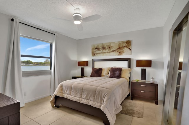 bedroom with ceiling fan, light tile patterned flooring, a water view, and a textured ceiling