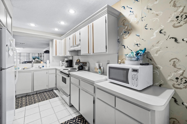 kitchen with a textured ceiling, light tile patterned floors, white cabinets, and white appliances