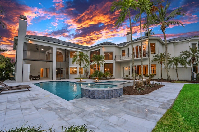 pool at dusk with an in ground hot tub and a patio