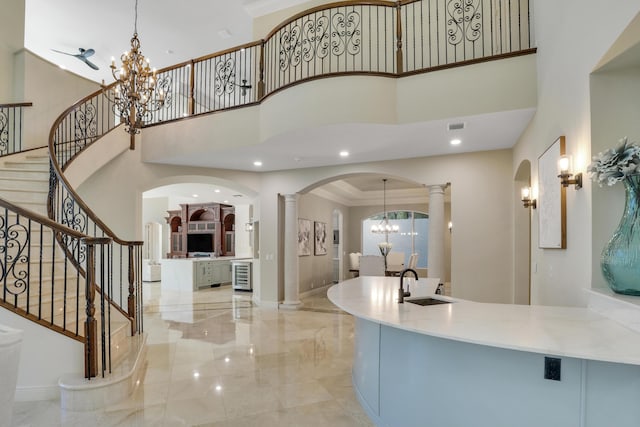 foyer entrance with a high ceiling, an inviting chandelier, crown molding, wine cooler, and sink