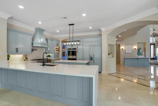 kitchen with pendant lighting, custom exhaust hood, sink, built in appliances, and kitchen peninsula