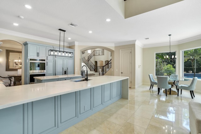 kitchen with a large island with sink, sink, paneled refrigerator, and decorative light fixtures