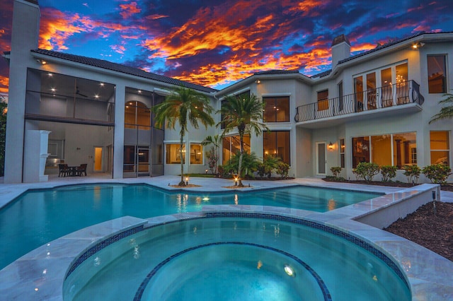 pool at dusk featuring a patio area and an in ground hot tub