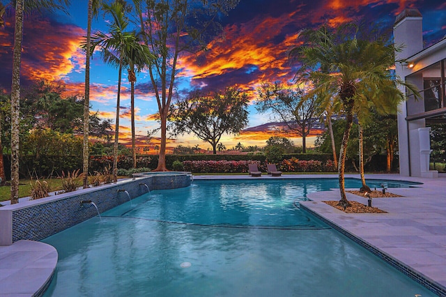 pool at dusk featuring pool water feature and a patio