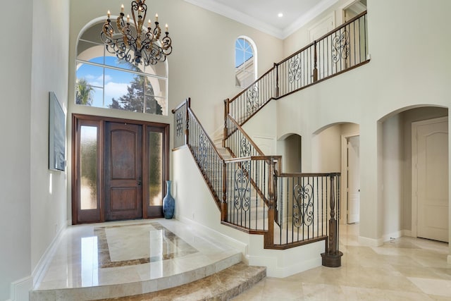 entryway featuring crown molding, a towering ceiling, and an inviting chandelier