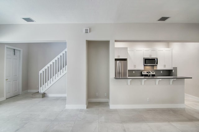 kitchen featuring a kitchen breakfast bar, kitchen peninsula, appliances with stainless steel finishes, tasteful backsplash, and white cabinetry