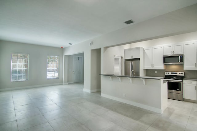 kitchen featuring a kitchen breakfast bar, decorative backsplash, light tile patterned floors, white cabinetry, and stainless steel appliances