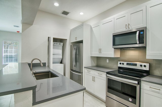 kitchen with sink, stacked washing maching and dryer, light tile patterned flooring, white cabinetry, and stainless steel appliances