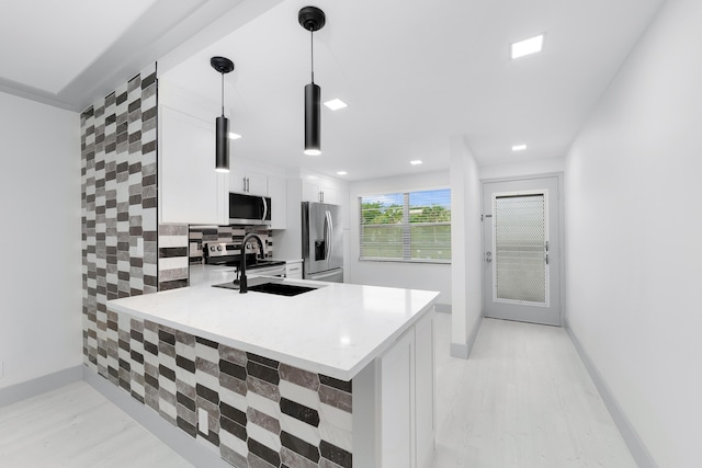 kitchen featuring sink, kitchen peninsula, appliances with stainless steel finishes, decorative light fixtures, and white cabinetry