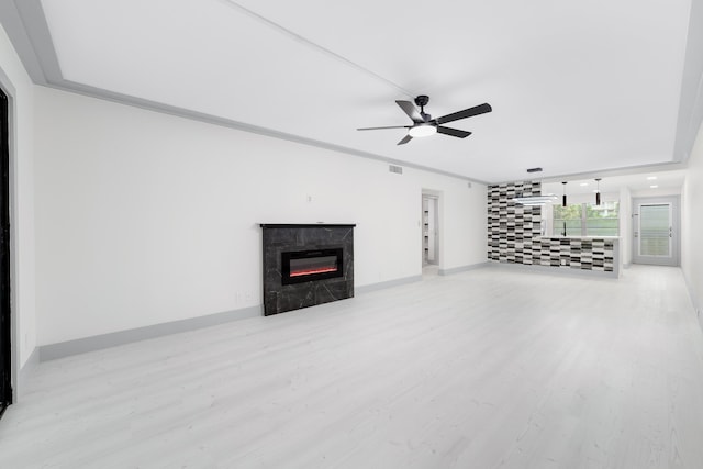 unfurnished living room featuring ceiling fan, a premium fireplace, crown molding, and light hardwood / wood-style flooring