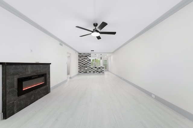 unfurnished living room with ceiling fan, a tiled fireplace, crown molding, and light hardwood / wood-style flooring