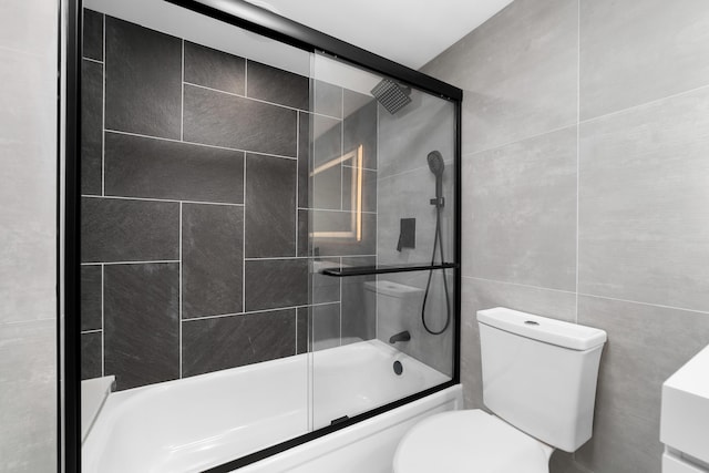 bathroom featuring toilet, tile walls, and combined bath / shower with glass door