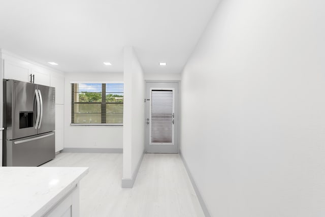 kitchen with white cabinets, light stone counters, stainless steel refrigerator with ice dispenser, and light hardwood / wood-style flooring