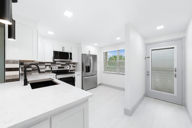 kitchen with decorative backsplash, appliances with stainless steel finishes, light stone counters, sink, and white cabinets