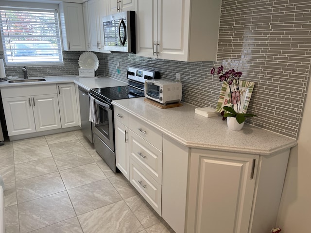 kitchen featuring tasteful backsplash, stainless steel appliances, sink, light tile patterned floors, and white cabinets